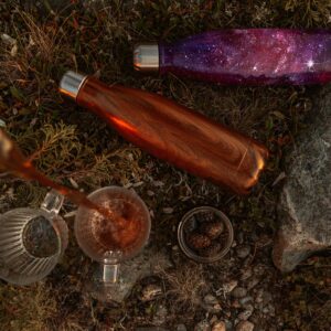 Pouring tea into a glass outdoors with thermos flasks on the ground.